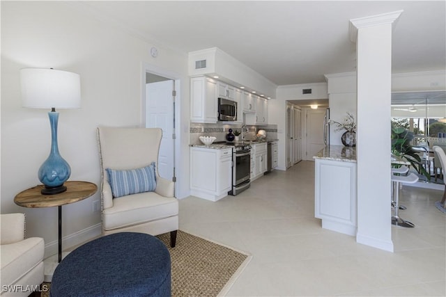 kitchen with crown molding, appliances with stainless steel finishes, white cabinetry, backsplash, and light stone countertops