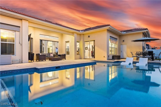 pool at dusk with an outdoor living space and a patio area