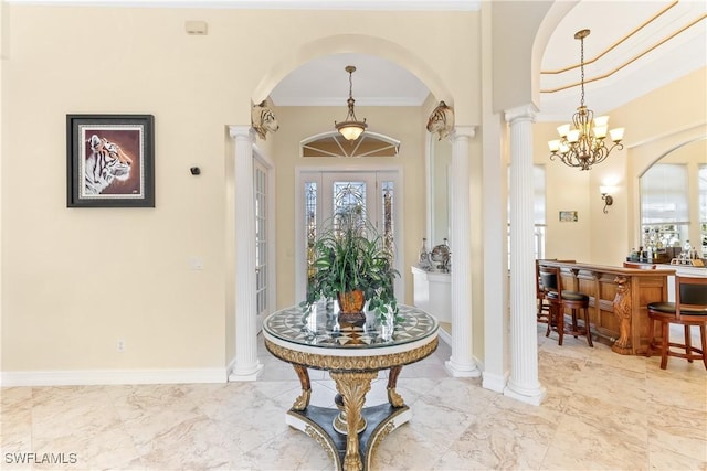 foyer entrance featuring a notable chandelier, bar, ornamental molding, and decorative columns