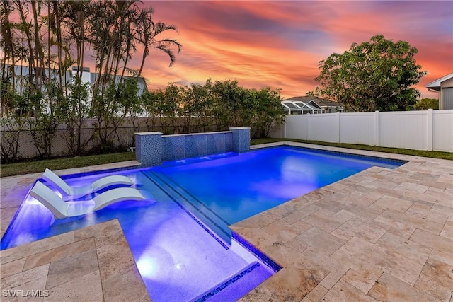 pool at dusk with pool water feature and a patio