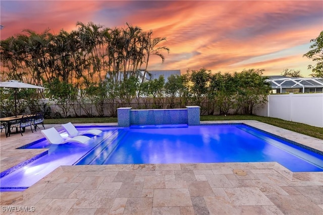 pool at dusk featuring pool water feature and a patio