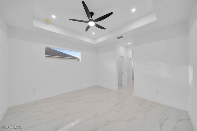 empty room with ceiling fan and a raised ceiling