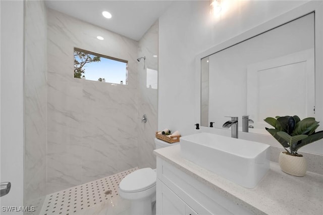 bathroom with toilet, a tile shower, and vanity