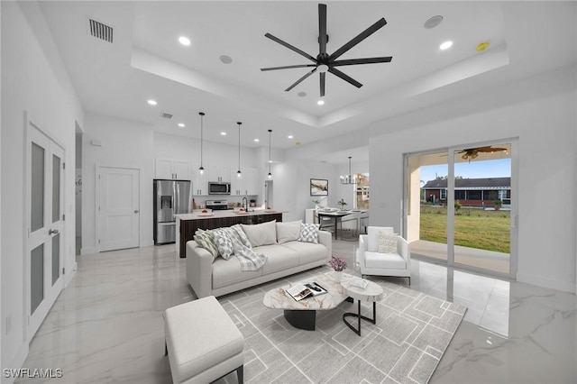 living room with ceiling fan with notable chandelier, sink, and a raised ceiling