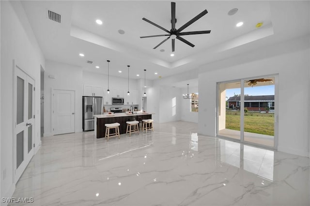 interior space featuring appliances with stainless steel finishes, pendant lighting, a raised ceiling, and a kitchen island