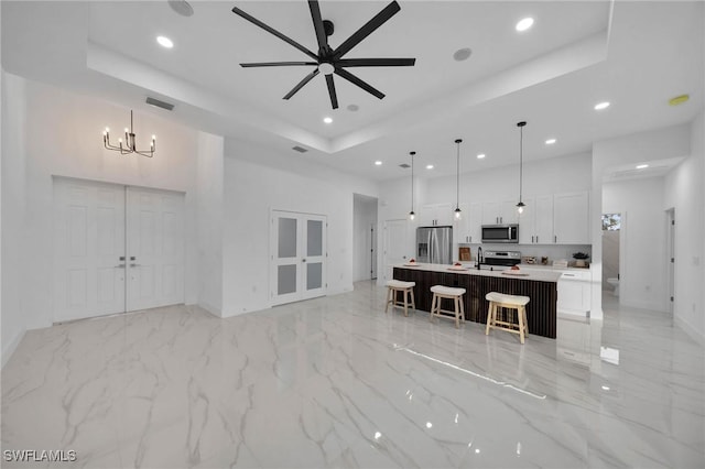 living room with ceiling fan with notable chandelier and a tray ceiling