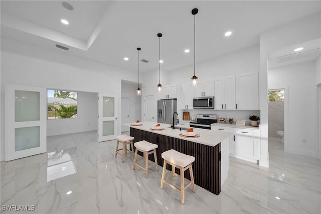 kitchen with hanging light fixtures, a kitchen island with sink, appliances with stainless steel finishes, a kitchen breakfast bar, and white cabinets