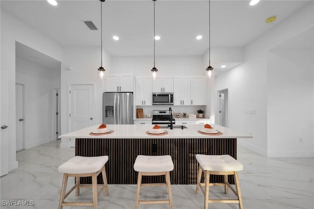 kitchen with hanging light fixtures, white cabinets, a kitchen island with sink, and stainless steel appliances