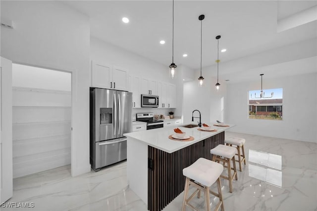 kitchen with appliances with stainless steel finishes, white cabinetry, hanging light fixtures, a center island with sink, and a breakfast bar area