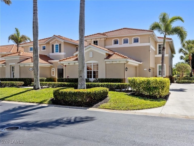 mediterranean / spanish-style house with driveway, a front lawn, a tile roof, and stucco siding