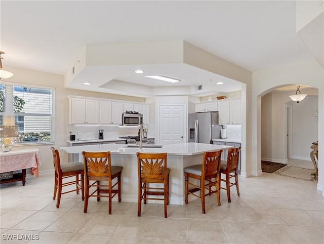 kitchen featuring white cabinets, appliances with stainless steel finishes, a raised ceiling, light countertops, and arched walkways