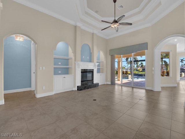 unfurnished living room featuring crown molding, ceiling fan, a tray ceiling, a fireplace, and built in shelves