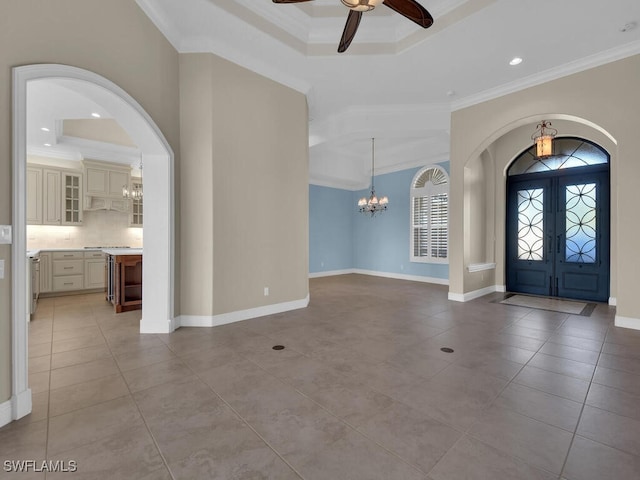 tiled foyer featuring a tray ceiling, ceiling fan with notable chandelier, ornamental molding, and french doors