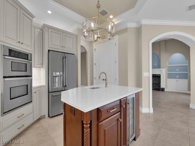 kitchen featuring sink, crown molding, appliances with stainless steel finishes, a kitchen island with sink, and beverage cooler