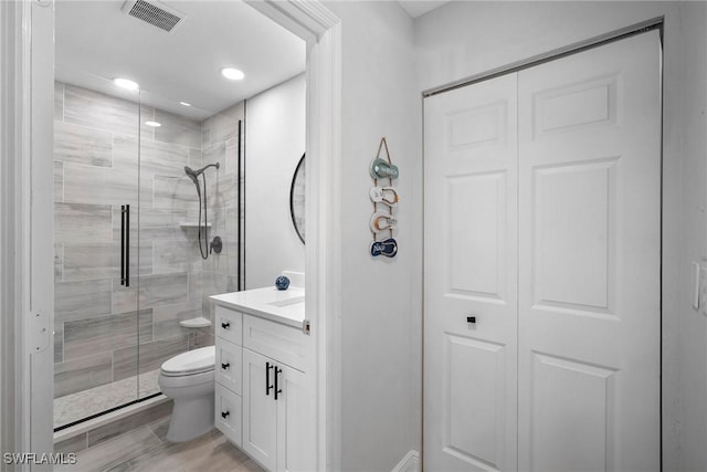 bathroom with a shower with door, vanity, and toilet