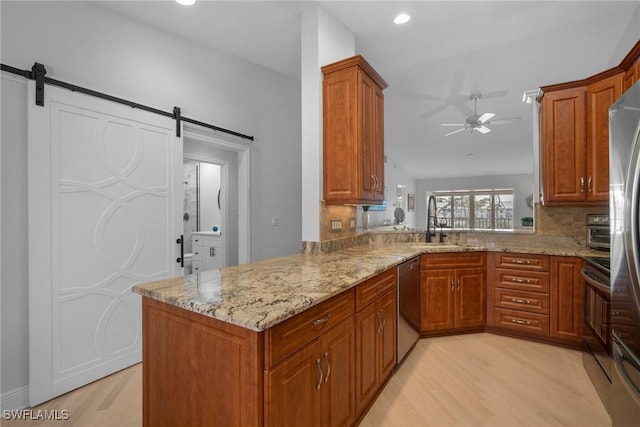 kitchen featuring light stone countertops, stainless steel appliances, kitchen peninsula, and a barn door