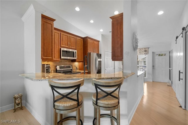 kitchen with stainless steel appliances, a barn door, kitchen peninsula, and a breakfast bar