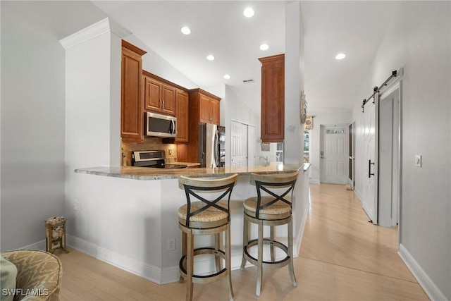 kitchen with stainless steel appliances, light hardwood / wood-style floors, kitchen peninsula, a kitchen bar, and a barn door