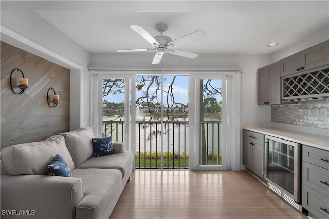 interior space with ceiling fan, a water view, bar area, beverage cooler, and light wood-type flooring