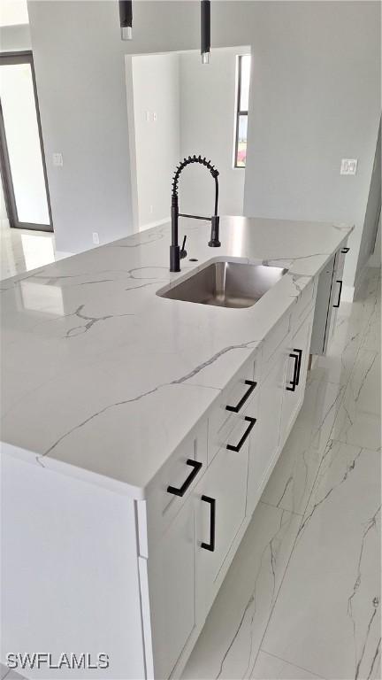 kitchen with a kitchen island, sink, white cabinets, and light stone countertops