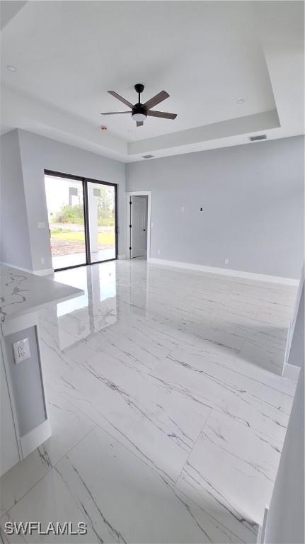 empty room with ceiling fan and a tray ceiling