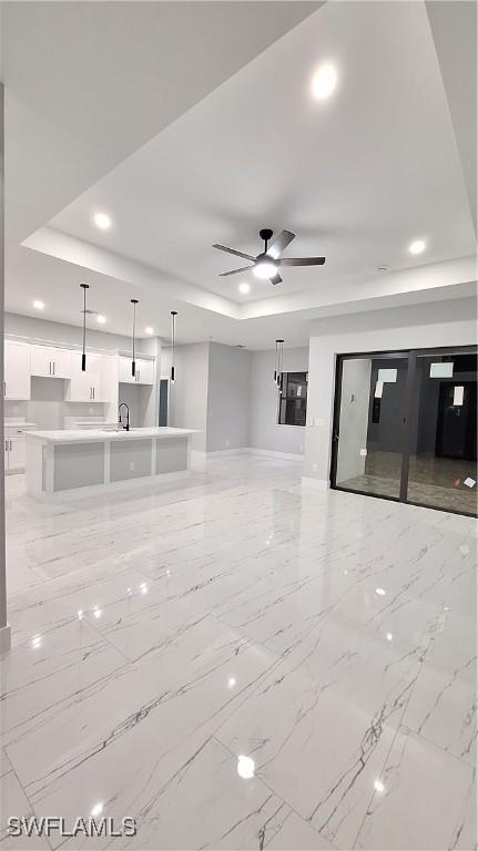 unfurnished living room featuring a tray ceiling, marble finish floor, a sink, and ceiling fan