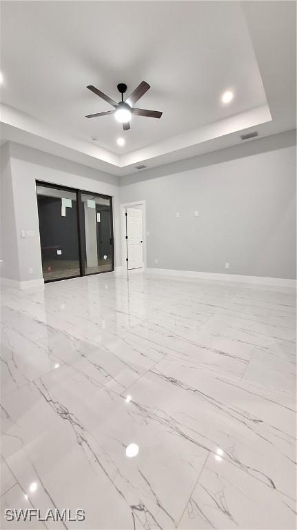 unfurnished living room with marble finish floor, a raised ceiling, visible vents, a ceiling fan, and baseboards