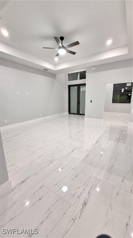 unfurnished living room with recessed lighting, a ceiling fan, baseboards, marble finish floor, and a raised ceiling