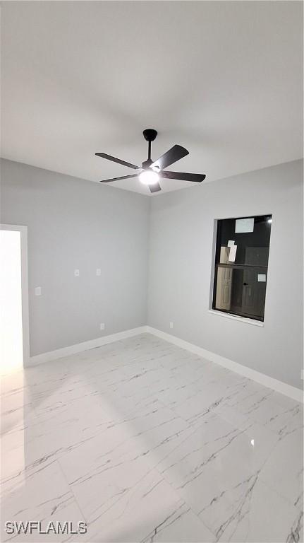 spare room with marble finish floor, a ceiling fan, and baseboards