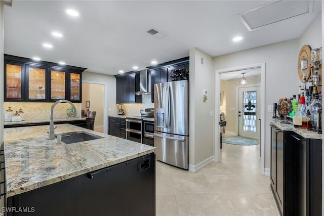 kitchen with sink, wall chimney range hood, appliances with stainless steel finishes, backsplash, and light stone counters