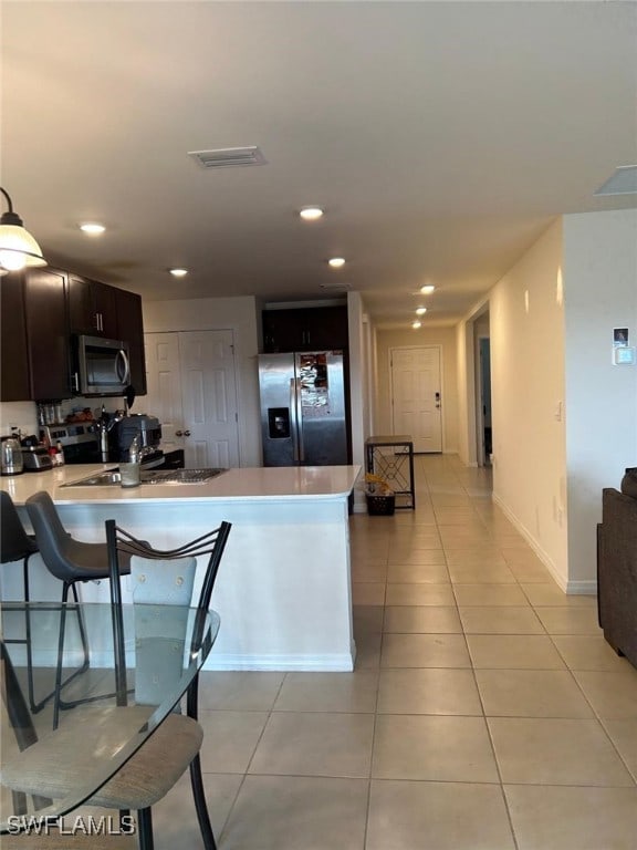 kitchen featuring kitchen peninsula, appliances with stainless steel finishes, light tile patterned flooring, and dark brown cabinetry