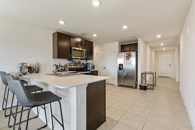 kitchen with sink, dark brown cabinets, appliances with stainless steel finishes, a kitchen breakfast bar, and kitchen peninsula