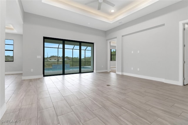 empty room with ceiling fan, a wealth of natural light, and a tray ceiling