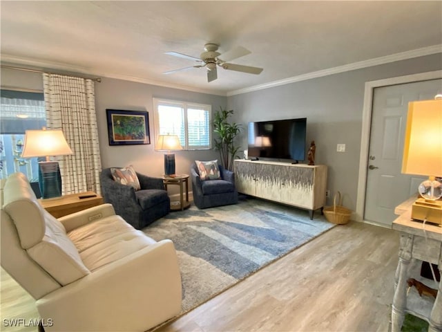 living room featuring wood-type flooring, ornamental molding, a large fireplace, and ceiling fan