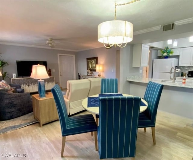 dining room with crown molding, ceiling fan, sink, and light hardwood / wood-style flooring