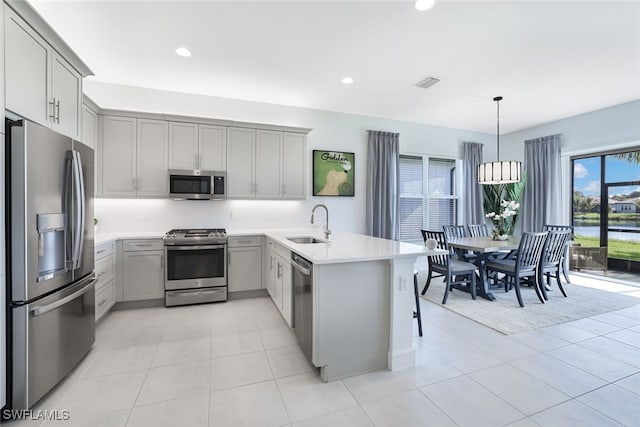 kitchen featuring pendant lighting, kitchen peninsula, appliances with stainless steel finishes, and gray cabinets