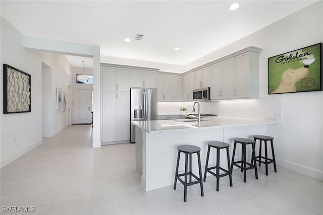 kitchen with appliances with stainless steel finishes, sink, gray cabinets, kitchen peninsula, and a breakfast bar area