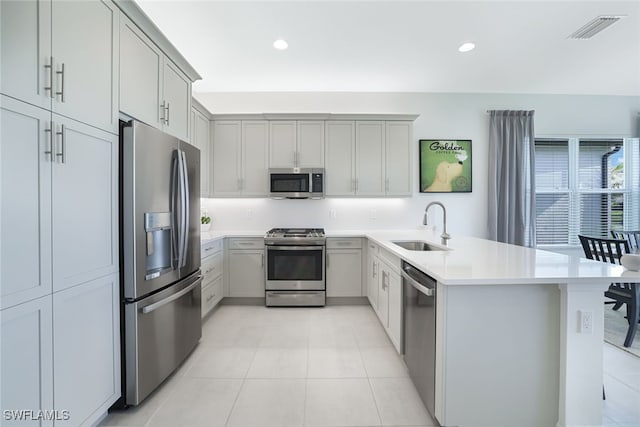 kitchen with kitchen peninsula, sink, gray cabinetry, light tile patterned floors, and stainless steel appliances