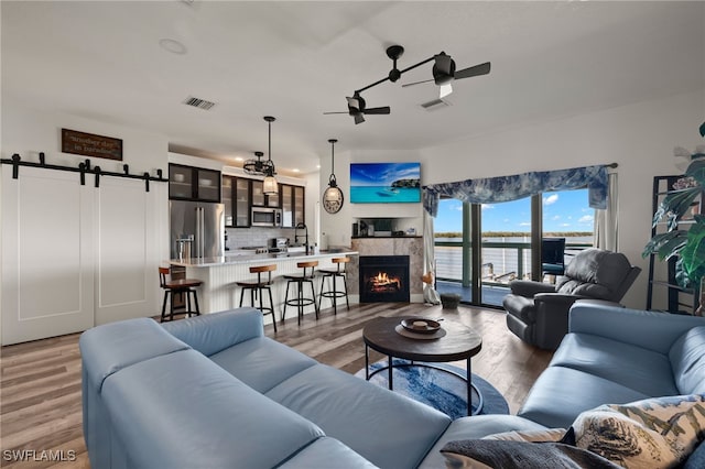 living room with light wood-type flooring, a barn door, ceiling fan, and a water view