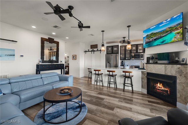 living room featuring sink, light hardwood / wood-style flooring, ceiling fan, a tiled fireplace, and a barn door