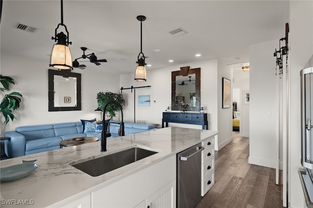 kitchen with white cabinetry, sink, hanging light fixtures, light stone counters, and a barn door