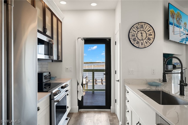 kitchen featuring appliances with stainless steel finishes, sink, white cabinets, decorative backsplash, and light stone counters