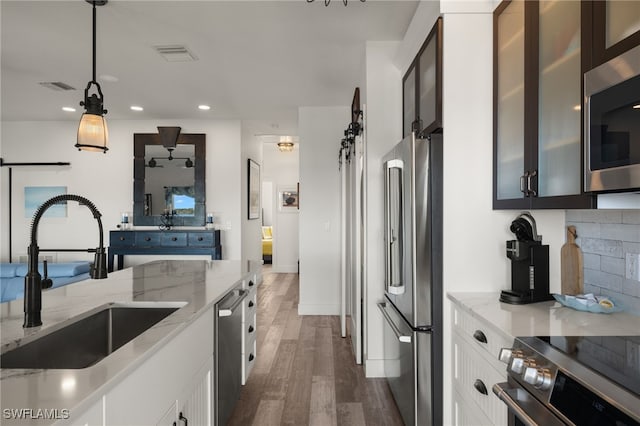 kitchen with sink, appliances with stainless steel finishes, hanging light fixtures, light stone countertops, and white cabinets