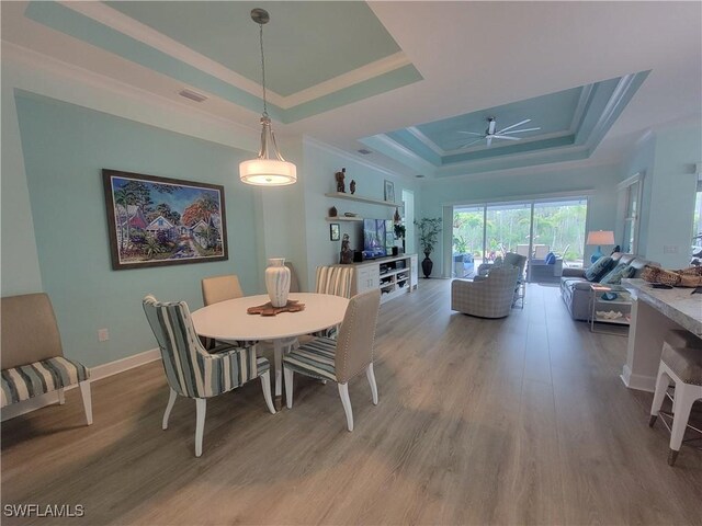 dining area featuring ceiling fan, a tray ceiling, and light wood-type flooring