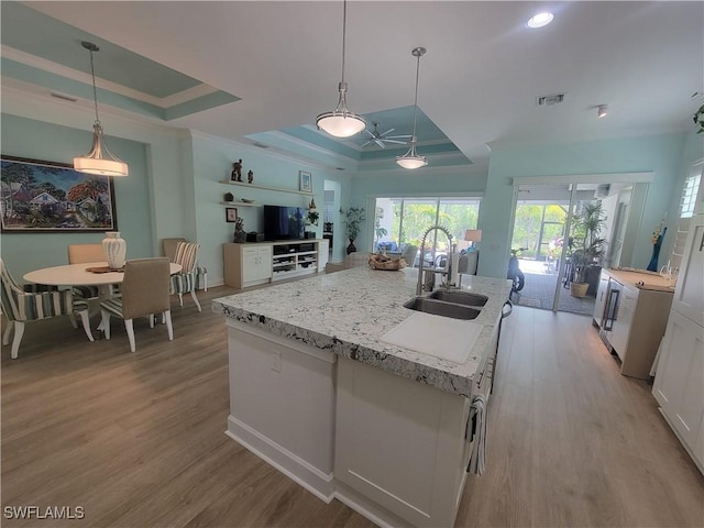 kitchen with decorative light fixtures, a raised ceiling, an island with sink, and white cabinets