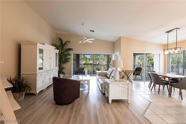 living room featuring ceiling fan with notable chandelier, light hardwood / wood-style flooring, and vaulted ceiling