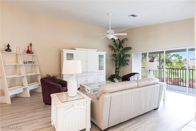 living room with visible vents, ceiling fan, light wood-style floors, and a towering ceiling