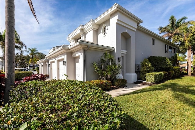 view of side of property featuring stucco siding, a lawn, and an attached garage