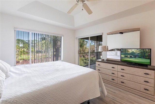 bedroom featuring a ceiling fan, access to exterior, wood finished floors, and a tray ceiling