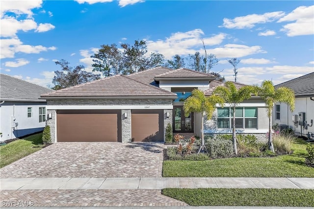 prairie-style home with an attached garage, decorative driveway, french doors, a front lawn, and stucco siding